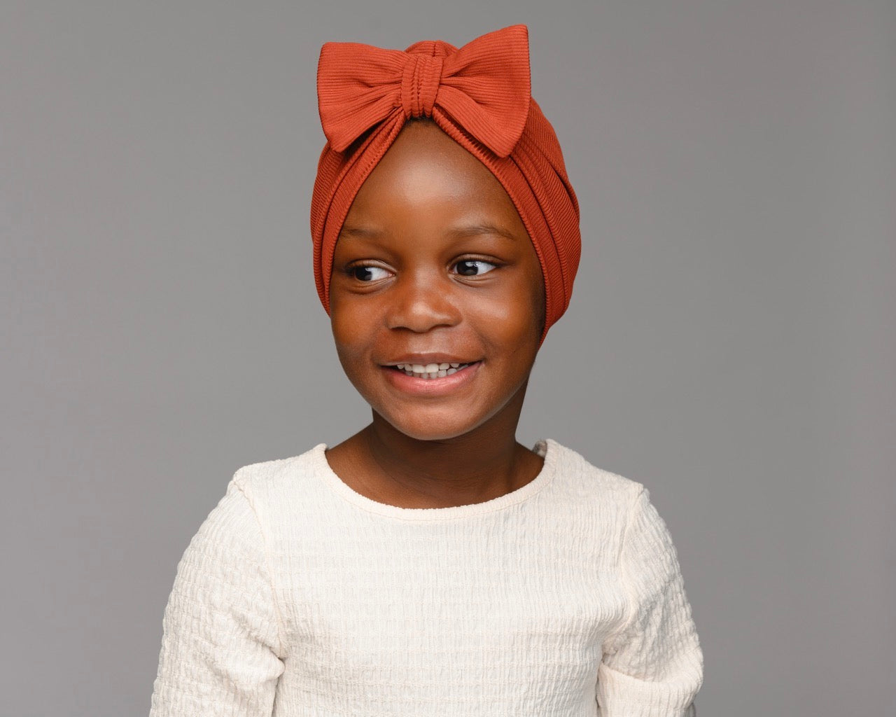 Child model wearing auburn turban with a bow