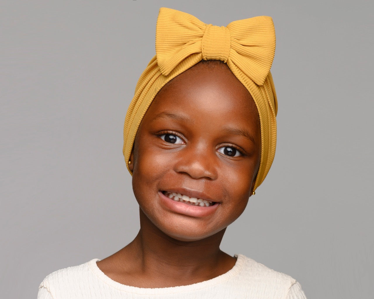 Child infant girl wearing a mustard satin-lined turban with a bow